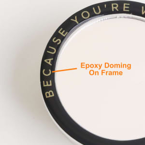 A custom-shaped mirror phone pop holder with a black frame and an epoxy domed finish. It features a logo on the edge.