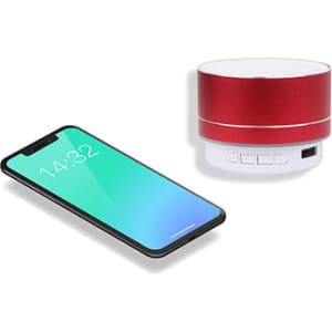 A red metal Bluetooth speaker beside a smartphone displaying a green gradient screen. The speaker features control buttons.