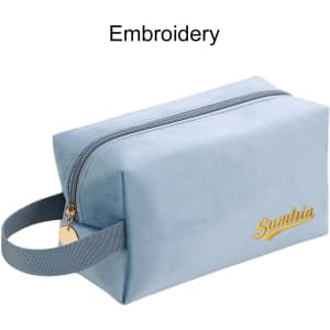 A light blue flannel cosmetic bag with a gold embroidered logo and a handle on one side.
