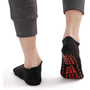 Low cut black kids' gripper socks with a red traction pattern on the sole, displayed on a person's feet.