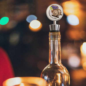 A drink bottle with a silver wine stopper featuring a logo design and a decorative top.