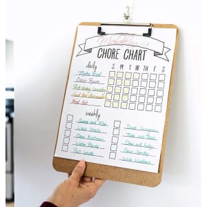 A wooden clipboard featuring a chore chart with colourful sections for daily and weekly tasks. It has a clip at the top.