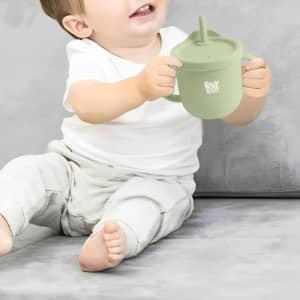 A drink bottle in soft green silicone, featuring a lid with a straw and a logo, held by a smiling child.