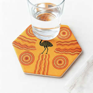A hexagonal ceramic coaster in orange and yellow with a decorative pattern and a glass of water on top.