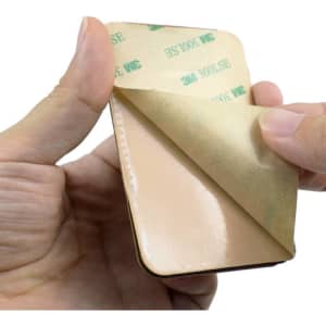 A PU phone stand card holder in tan colour being held, with an adhesive backing partially peeled away.