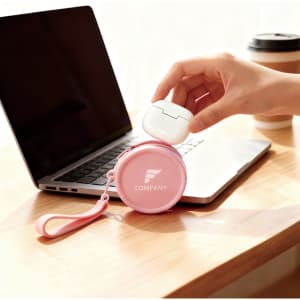 A round pink silicone coin pouch with a strap sits on a desk beside a laptop and a coffee cup.