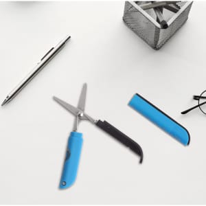 Multifunctional scissors with a blue handle, alongside a silver pen, a black ruler, and glasses on a light surface.
