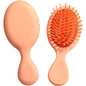 A mini paddle brush in a soft peach colour with plastic bristles and an ergonomic handle. It has a simple logo.