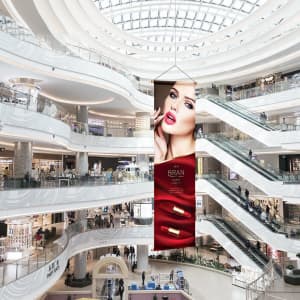 A hanging banner featuring a model with bold red lips and lipstick, displayed in a modern shopping centre.