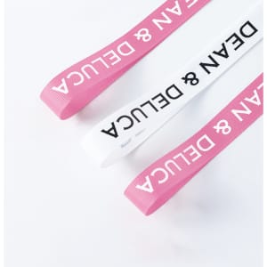 Ribbed fabric ribbon in pink and white, featuring a logo, suitable for various decorative uses.