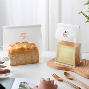 Clear sealing storage bags in a white and orange design, containing loaves of bread on a wooden tray.