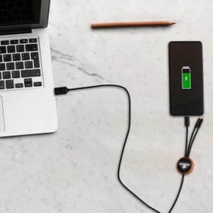 A round-shaped, long light-up charging cable connects a laptop to a smartphone on a marble surface.
