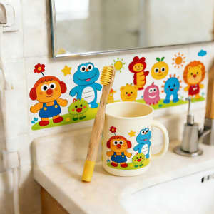 A bamboo toothbrush with a small round handle in a bathroom setting, alongside a colourful mug and cheerful wall stickers.