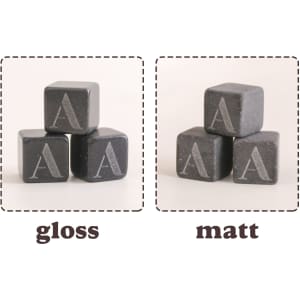 A set of black whiskey stones with engraved letters in gloss and matt finishes, shaped as square cubes.