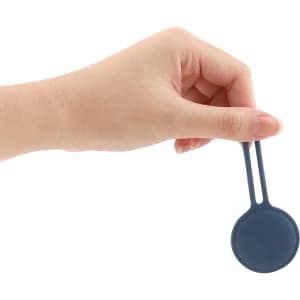A hand holding a dark blue Air Tag protective case with a flat, rounded design and a attaching loop.