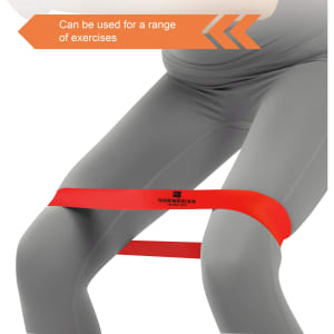 A red latex-free TPE fitness resistance band positioned around the thighs of a person wearing grey leggings.