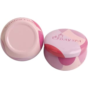 Two pink tin candles with a decorative design, featuring a logo on the lid.