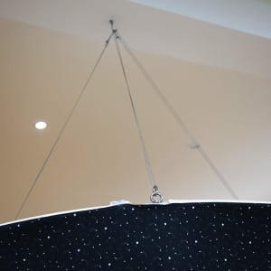 A round hanging banner in black with a patterned surface, suspended by metallic wires from the ceiling.