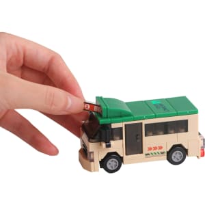 A hand adjusts a green and beige building block bus model, featuring wheels and a roof sign.