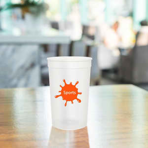 A translucent plastic stadium cup in clear colour with an orange splash logo, positioned on a wooden table.
