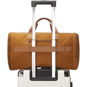 A foldable travel duffle bag in brown, sitting atop a wheeled suitcase with a retractable handle.
