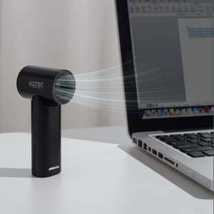 A black handheld fan with a sleek design, positioned next to a laptop on a desk. It features a logo.