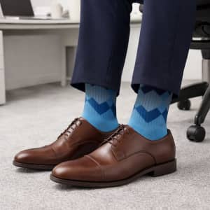 Brown dress shoes paired with blue patterned woven socks, worn with navy trousers in an office setting.