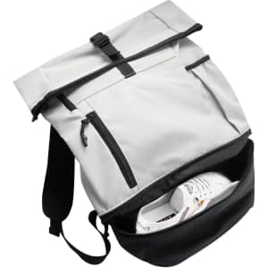A grey and black roll-top backpack with zippered pockets, featuring a pair of white sneakers inside.