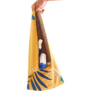 A hand holds a yellow bag with a tropical design containing various bottles inside.