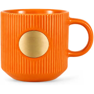 An orange ceramic mug with a textured surface and a bronze medal accent. Features a single handle and a round base.