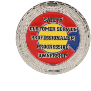 A commemorative gold coin pin with a red, blue, and yellow design featuring various phrases and a decorative border.