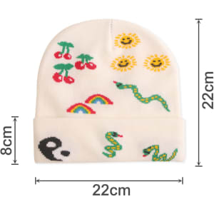 A white knitted beanie with colourful designs featuring cherries, suns, rainbows, and snakes, along with a logo.