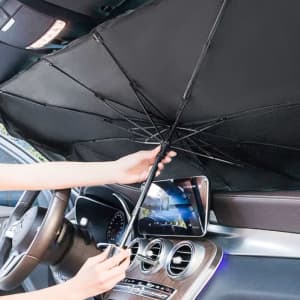 A black car shade umbrella being opened inside a vehicle, with a phone propped up on the dashboard.