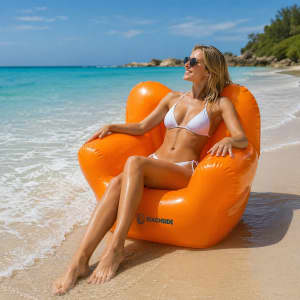 An inflatable chair in bright orange sits on the beach, with a woman in a white bikini lounging comfortably.