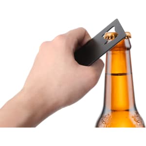 A drink bottle opener shaped like a card, in a sleek black finish, being used to open a beer bottle.