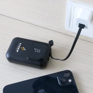 A black 10000mAh eco portable fast charging power bank connected to a charger, with a smartphone nearby.
