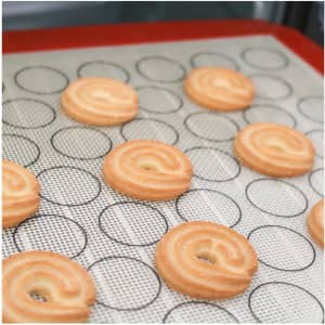 A silicone baking mat with a red border and circular markings, featuring freshly piped pastry swirls.