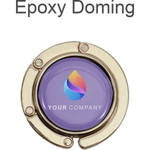 A round, foldable desk hook in gold with a purple center featuring a logo.