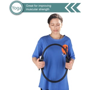 A woman holds a black Pilates Circle, wearing a blue shirt. The product is designed for strength training.