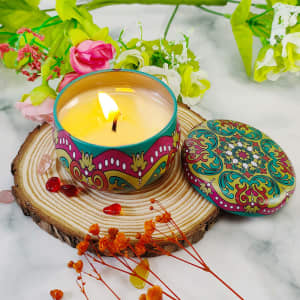 A decorative tin candle with a colourful floral design, surrounded by flowers and natural wood elements.