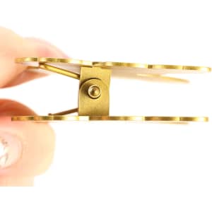 A custom metal clip with a shiny gold finish, held between fingers, showcasing its design and hinge mechanism.