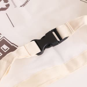 A reusable linen bread bag in a beige hue, featuring a black buckle on a strap. It has a logo printed on the surface.