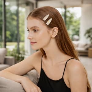 A model with long, straight brown hair wears two beige acetate hair alligator clips in her hair, set against a bright, airy background.