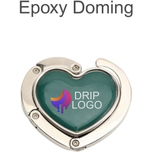 A heart-shaped, foldable desk hook in silver with a green epoxy finish and a logo.