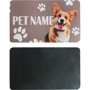 A pet feeding mat with a smiling dog illustration and paw prints, featuring a textured black reverse side.