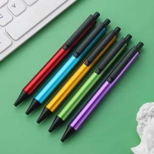A selection of six plastic click pens in red, blue, yellow, green, and purple, with black tips and grips.