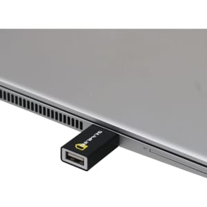 A black USB data blocker is plugged into a silver laptop, highlighting its sleek and compact design.