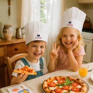 A white non-woven kids chef hat with a logo, worn by two children at a table with pizza and drinks.