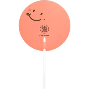 A round, orange hand fan with a smiling face design and a white handle, featuring a logo and text.