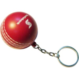 A red cricket ball stress reliever attached to a metal keyring, featuring a logo on its surface.